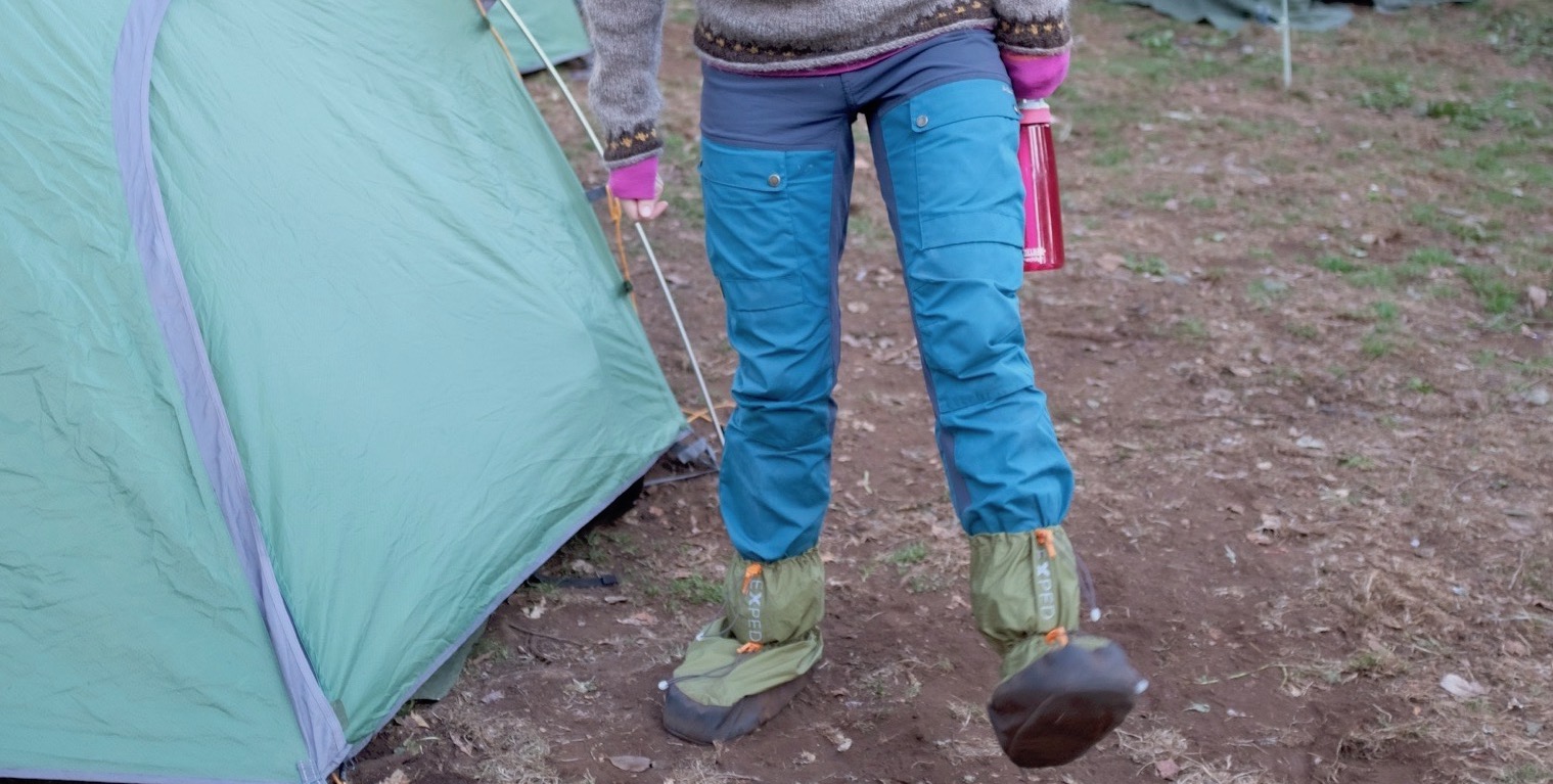 Beina mine, ved siden av et grønt telt. Jeg har på meg en blå turbukse, og posesokker nederst på beina. Man kan såvidt se litt av armene mine, og i den ene hånda holder jeg en rosa drikkeflaske.
